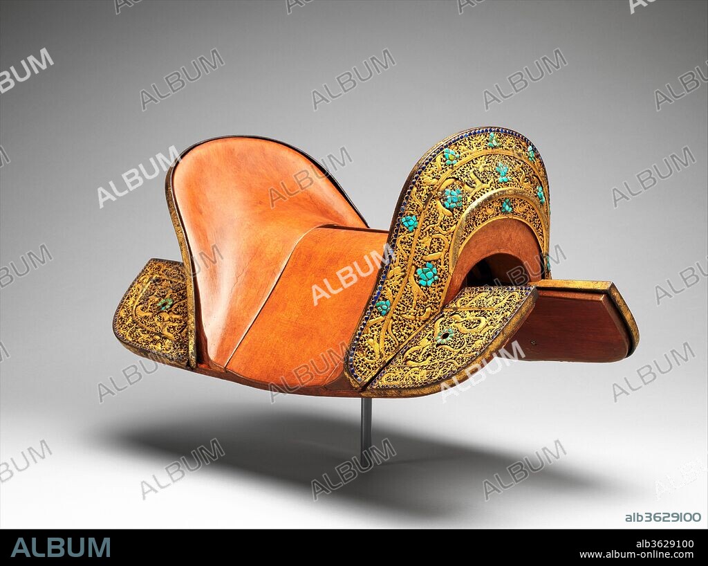 Set of Saddle Plates. Culture: Tibetan or Chinese. Dimensions: H. 10 7/8 in. (27.6 cm); L. 23 1/2 in. (59.7 cm); W. 13 3/4 in. (34.9 cm). Date: ca. 1400.
This set of saddle plates represents a high point in the medium of pierced ironwork, equaling or excelling anything of its type. Each plate is chiseled from a single piece of iron. The long, thin four-clawed dragons, carved in high relief in great detail, are cut entirely free from the surrounding scrollwork ground so that they can move slightly within it. The scroll patterns are undercut to give the appearance of depth and overlap, in addition to the areas where the bodies of the dragons actually do overlap. There is a Wish-Granting Jewel motif made with pieces of blue and green turquoise set in shaped compartments in the center of both the pommel and the cantle, and scattered lotus blossoms made in the same way. The outer edges of the plates are bordered by rows of semicircular pieces of lapis. The iron surfaces of the plates are damascened completely with gold foil, and the precision and fineness of the cross-hatching beneath the gold are exceptional.