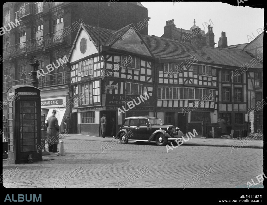 GEORGE BERNARD WOOD. Old Wellington Inn, Old Shambles, Manchester, 1942. An exterior view of the Old Wellington Inn, showing the front facade in Old Shambles. The former house, now public house, dates to the mid 16th century, and was altered and raised by 30ft in the 1970s. It was moved c70m north to its current position, alongside Sinclairs Oyster Bar, in the mid to late 1990s, opening again in 1999. The inn has three storeys and a three bay plan, with the end bays gabled. There is a splayed door in the left corner, and a 20th century door in the centre of the south facade. The photo shows the inn in it's original setting, on Old Shambles. It was moved after an IRA bombing in 1996.