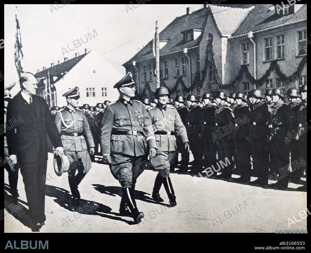 SS-group leader and lieutenant general of the Waffen-SS Jüttner proceeds after the swearing in front of the volunteer battalion from beside him ( in civil ) Vidkun . Quisling and ( with a helmet ) of the battalion commander , the Norwegian major Bakke. Taken during the occupation of Norway, 1940.
