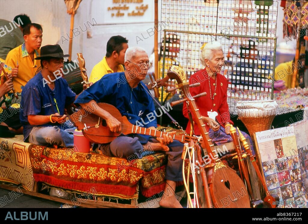 Thailand: A group of traditional Thai musicians known as a <i>wong khrueang sai</i> (string ensemble) entertain the general public at Chiang Mai's famous Sunday Walking Street Market.<br/><br/>. A typical <i>khrueang sai</i> ensemble features two two-string fiddles, one high and one low (<i>saw duang</i> and <i>saw u</i>), a three-string zither called <i>jakhe</i>, a vertical duct flute called <i>khlui</i>, hand drums, and various <i>ching</i> or cymbals. Depending on the size of the ensemble, instruments may be doubled or left out.