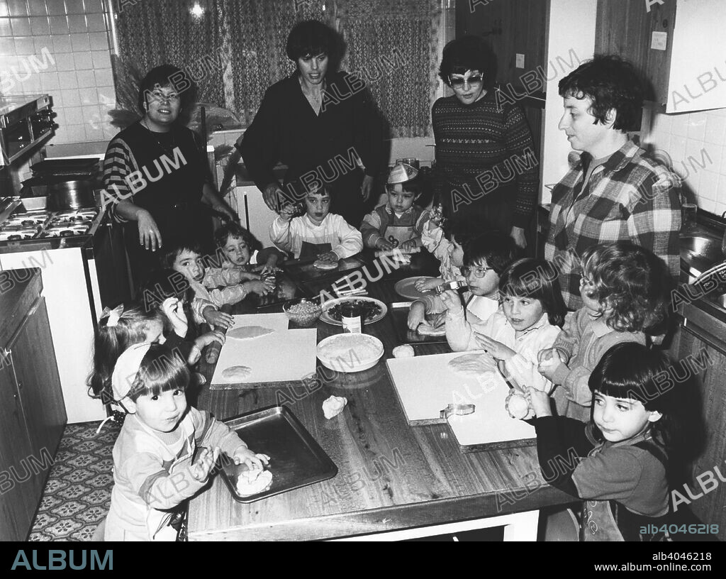 Teacher Janet Lawson demonstrates kichal baking, Gan Yeladim Synagogue kitchen, Reading, 1987. A class of children learns to bake special food for a Jewish religious festival. From front left: Neil Clarke, Galia Rosen, Katie Gordon, Rachael Lyons, Supervisor Hilary Meyer, Naomi Firsht, Rachel Firsht, Supervisor Janet Lawson, Alexander Ruben, helper Carole Gold, Shoshana Ross, Debbie Mayer, Jenny Gordon, helper and mother Judi Lyons, Jessica Lawson, Belinda Gold.