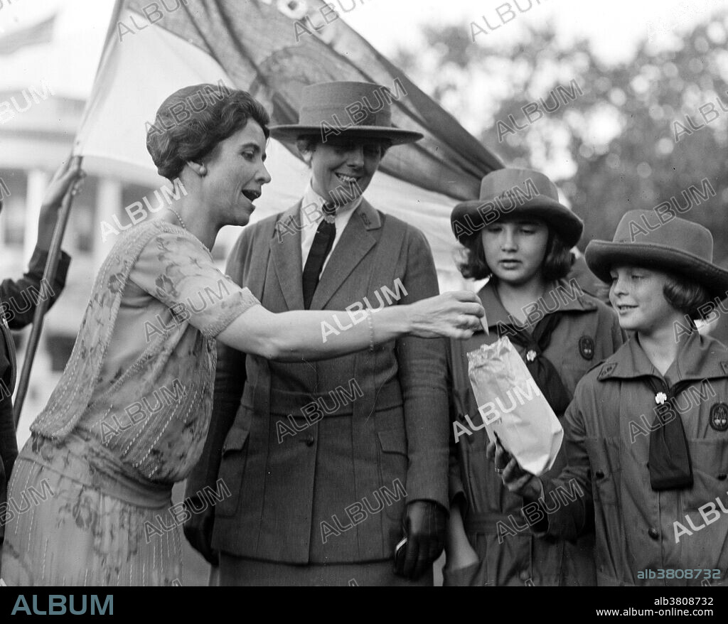 Mrs. Coolidge takes cookie from Girl Scouts. Grace Anna Goodhue Coolidge (January 3, 1879 - July 8, 1957) was First Lady from 1923-29. She graduated from the University of Vermont in 1902 and then joined the faculty of the Clarke School for the Deaf in Northampton, Massachusetts, as a lip reading instructor. She married Calvin Coolidge in 1905. She took her part in town activities, attended her church, and offset his shyness with a cheery friendliness. As First Lady, she was a popular hostess. The Coolidges were a particularly devoted couple, although the president never discussed state matters with her. Coolidge summed up his marriage to Grace in his autobiography: "For almost a quarter of a century she has borne with my infirmities, and I have rejoiced in her graces." After her husband's death, she continued her work on behalf of the deaf. She was also active in the Red Cross, civil defense, and scrap drives during WWII. She kept her sense of fun and her aversion to publicity until her death in 1957 at the age of 78. Photographed by the National Photo Company October 17, 1923.