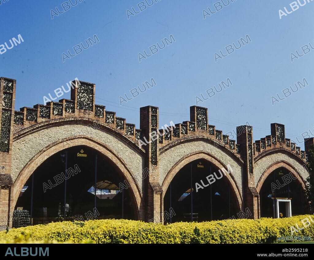 JOSEP PUIG I CADAFALCH. Cavas Codorniu, 1902-1915. Porche de las Prensas, actual Museo. Fachada con arcos apuntados y frontón escalonado. Uso del ladrillo, la piedra y el trencadís de cristal verde. Sant Sadurní d'Anoia.