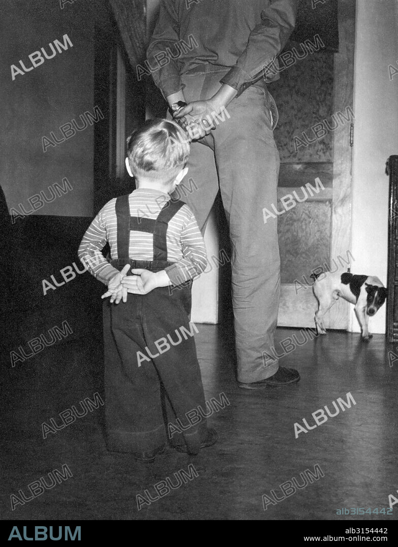 United States:  c. 1955. A small boy imitates his father's pose in confronting the 'bad dog'.