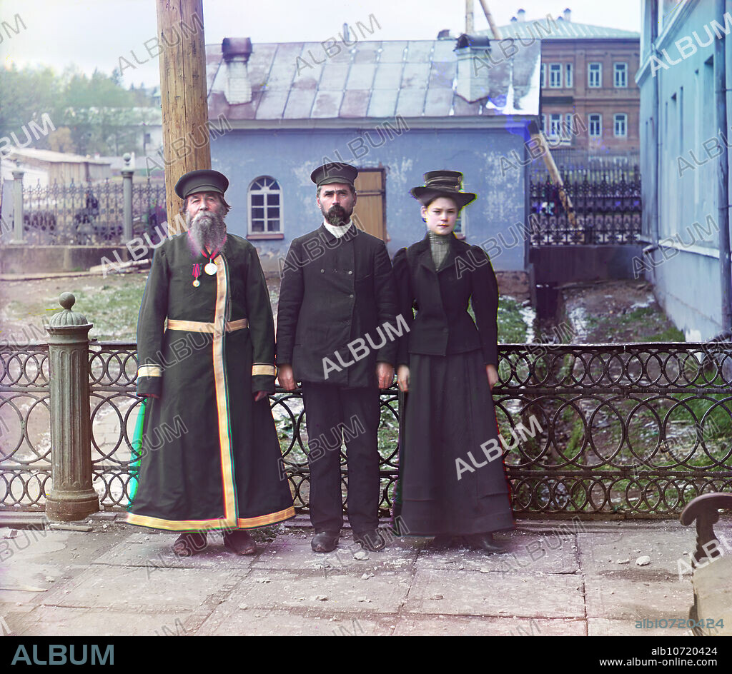 SERGEY MIKHAYLOVICH PROKUDIN-GORSKY. Three generations: A.P. Kalganov with son and granddaughter; the last two work in the shops of the Zlatoust plant, 1910. Two men and a woman posed outdoors at the Zlatoust arms plant. A. P. Kalganov poses with his son and granddaughter for a portrait in the industrial town of Zlatoust in the Ural Mountain region of Russia. The son and granddaughter are employed at the Zlatoust Arms Plant; a major supplier of armaments to the Russian military since the early 1800s. Kalganov displays traditional Russian dress and beard styles, while the two younger generations have more Westernized, modern dress and hair styles.