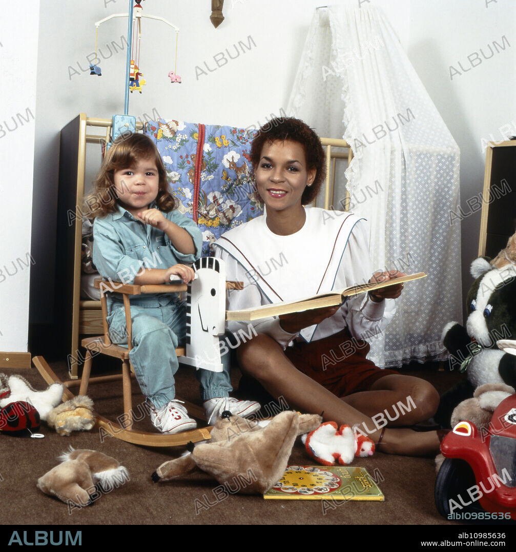 Homestory of the German pop, disco and pop singer Ramona Wulf with her daughter reading aloud in the children's room, Germany Berlin circa 1985.