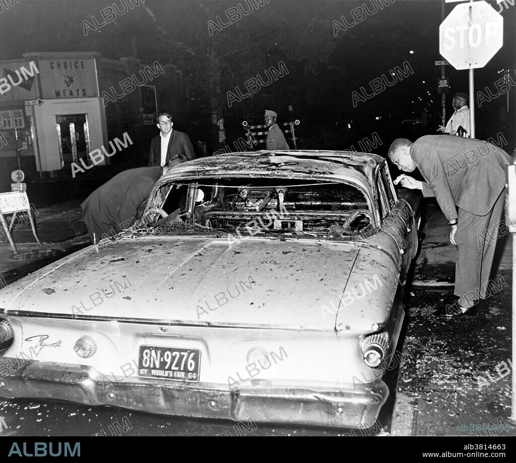 Entitled: "Detective examines burned out police car on Herkimer Street and Nostrand Avenue as the Harlem rioting fanned out to Brooklyn last night." On Thursday, July 16, 1964, James Powell was shot and killed by police Lieutenant Thomas Gilligan. The second bullet of three fired by Lieutenant Gilligan killed the 15-year-old African American in front of his friends and about a dozen other witnesses. The incident immediately rallied about 300 students from a nearby school who were informed by the principal. This incident set off six consecutive nights of rioting that affected the New York City neighborhoods of Harlem and Bedford-Stuyvesant. In total, 4,000 New Yorkers participated in the riots which led to attacks on the New York City Police Department, vandalism, and looting in stores. At the end of the conflict, reports counted one dead rioter, 118 injured, and 465 arrested. Photographed for the New York World-Telegram & Sun by Stanley Wolfson, 1964.