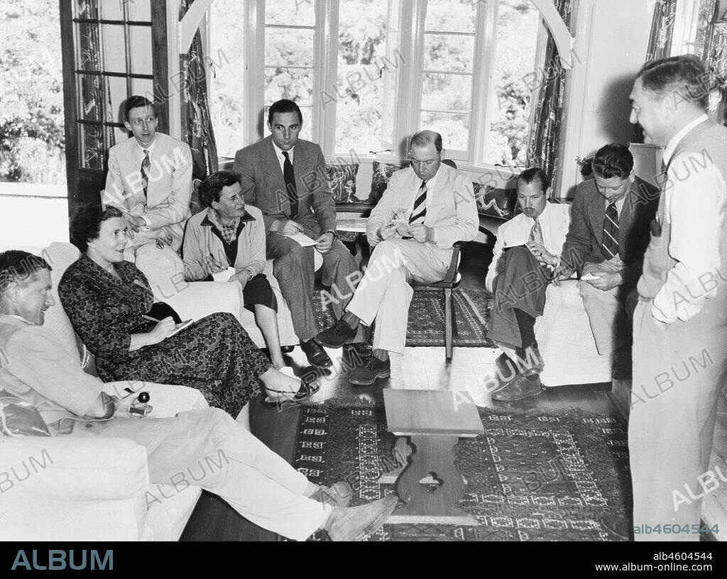 Kenya, A group of nine people in a room of the Sagana "Royal" Lodge who are engaged in writing down the news of the death of King George VI. A man who is standing appears to address the group. The Royal couple had been due to spend a holiday at the Lodge but left folllowing news of the King's death, February 1952. 2001/090/1/4/1/77.