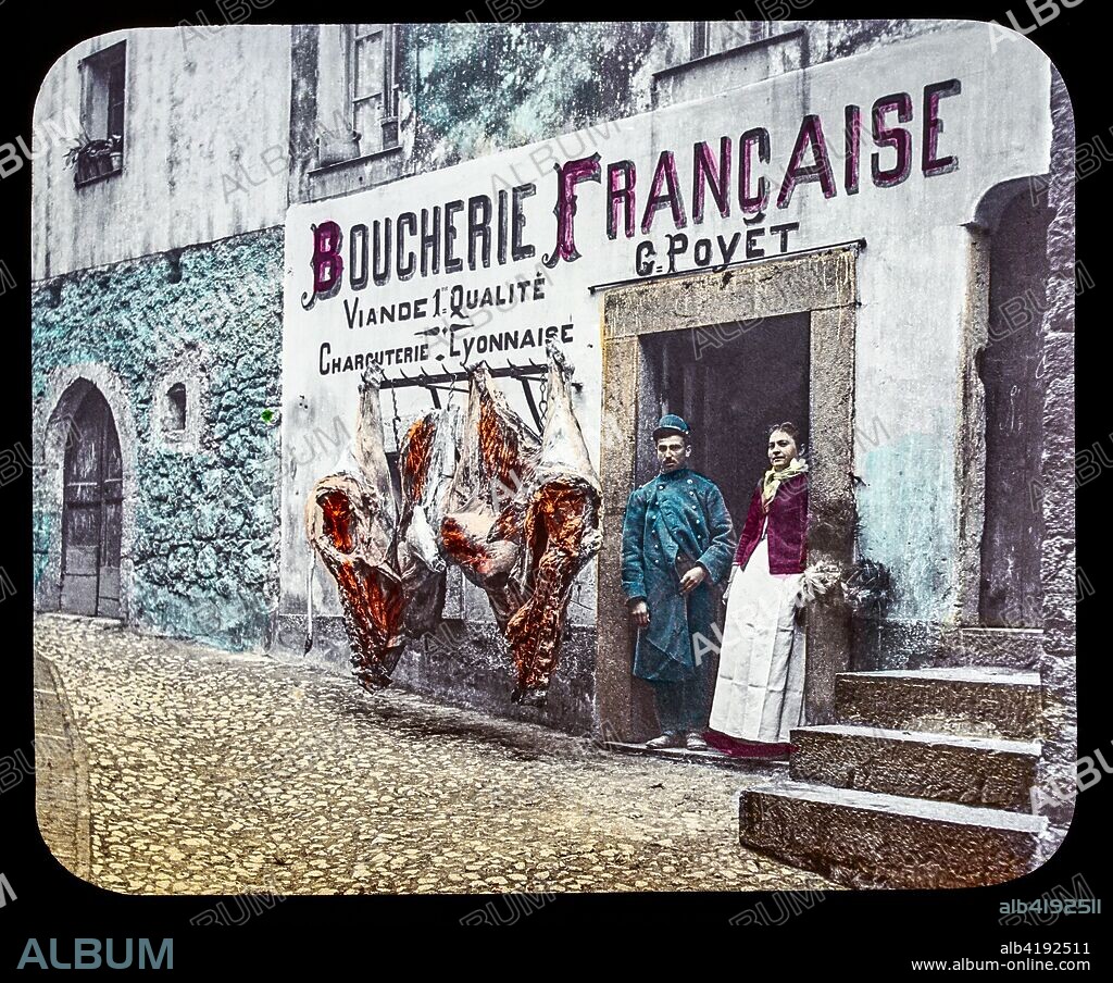Magic Lantern slide circa 1900. Victorian or Edwardian era. The origional monchrome ( black and white ) photograph hand coloured.The photograph is the work of G.W. Wilson photographer and slide manufacturer 1823-1893.George Washington Wilson (7 February 1823 - 9 March 1893)  was a pioneering Scottish photographer. The French Riviera and Monte Carlo (lecture ) .Slide 39 boucherie Francaise, G. Poyet La Turbie, Southern France. A man and woman at the shop door with meat hanging in the street.