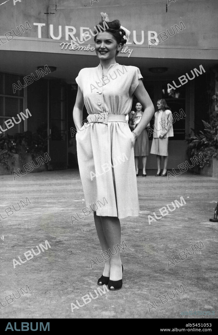 Track Suit -- Appropriately enough, this neat little number (the dress, of course) is named "Winning Time." Designed by Lynn Lester, California designer, it is modeled at Hollywood Park's exclusive Turf Club. The dress is of raw silk, has cap sleeves, slash pockets and leather-lined belt. Norma Crieger is the model. She wears a winning smile to match the dress. January 13, 1946. (Photo by Arthur Sasse, International News Photo).