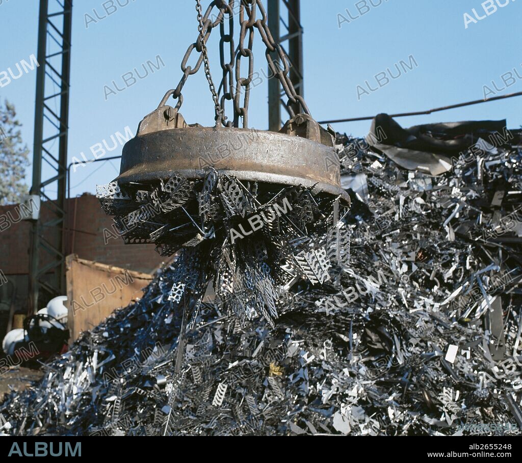 Electromagnet on crane lifting metal at scrap yard.