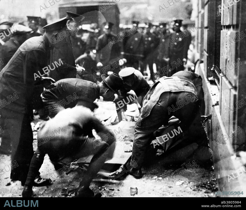 Entitled: "Picking up bodies following Wall St. explosion in 1920"." Police and others removing rubble to get to bodies lying underneath. On September 16, 1920, a horse drawn wagon stopped across the street from the headquarters of the J.P. Morgan bank at 23 Wall Street. Inside the wagon, 100 lbs of dynamite with 500 lbs of cast-iron sash weights exploded in a timer-set detonation. The horse and wagon were blasted into small fragments, but the driver was believed to have left the vehicle and escaped. The 38 victims, most of whom died within moments of the blast, were mostly young people who worked as messengers, stenographers, clerks, and brokers. The bomb caused more than $2 million in property damage ($23,500,000 with inflation) and destroyed most of the interior spaces of the Morgan building. There were 143 seriously injured, and the total number of injured was in the hundreds. The bombing was never solved, although investigators and historians believe the Wall Street bombing was carried out by Italian anarchists, a group responsible for a series of bombings the previous year. Photographed by the New York World-Telegram and the Sun Newspaper, 1920.