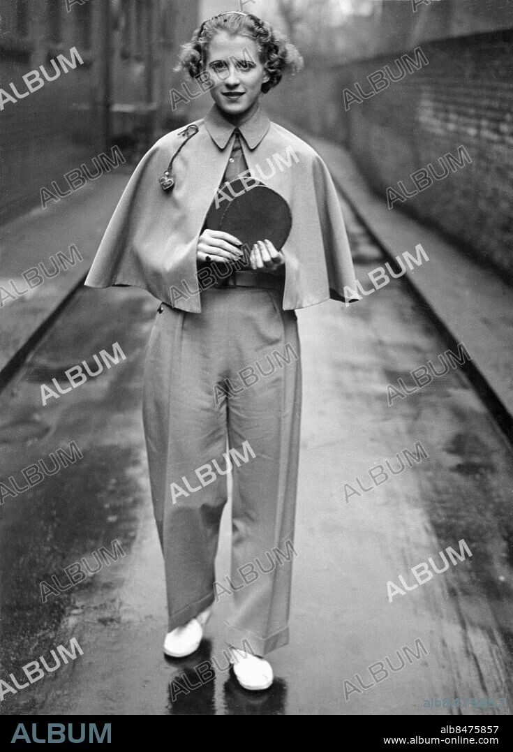 Orig. bildtext... WORLD CHAMPION SETS NEW FASHION. Miss Ruth Aarons, the blonde beauty from the U.S.A., who on Saturday won the British Table Tennis championship, after having won the world's championship, strikes a new fashion note with this smart outfit. It consists of tailored trousers, with blouse and cape to match. Anm. Bordtennis Världsmästare Racketar Långbyxor Cape Blondin Byxor Klackring CD499 persons: RUTH AARONS sites: STORBRITANNIEN;USA*.
