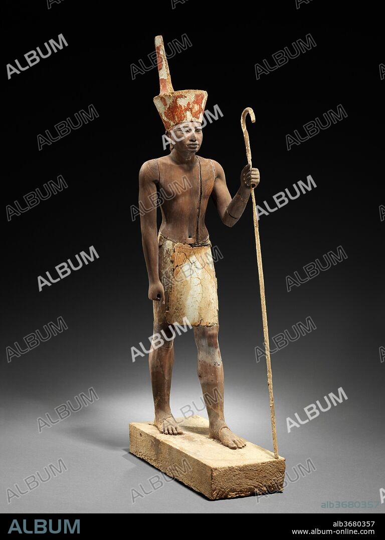 Guardian Figure. Dimensions: H. 57.6 cm (22 11/16 in.); W. 11 cm (4 5/16 in.); D. 26 cm (10 1/4 in.). Dynasty: Dynasty 12. Reign: reign of Amenemhat II. Date: ca. 1919-1885 B.C..
This figure wears the red crown of Lower Egypt and the face appears to reflect the features of the reigning king, most probably Amenemhat II or Senwosret II. However, the divine kilt suggests that the statuette was not merely a representation of the living ruler.  Together with its counterpart wearing the white crown of Upper Egypt, now in the Egyptian Museum, Cairo, the figure was discovered standing behind a shrine that contained an object sacred to the god Anubis, the so-called Imiut (14.3.18 and .19), and the two figures could be understood to have functioned as guardians of the Imiut. The ensemble was discovered in 1914 in the area surrounding the pyramid of Senwosret I at Lisht South during the Museum's excavation of a mud-brick enclosure surrounding the mastaba of Imhotep, a Twelfth Dynasty official. A chamber had been built into the south part of the enclosure wall and in it the statuettes and shrine were hidden, doubtlessly after having played a part in a dramatic funerary ceremony.