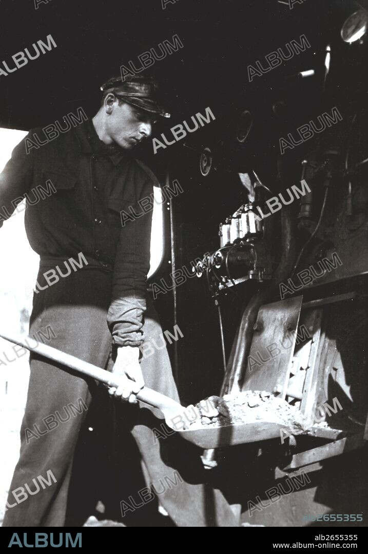 Fogonero echando carbón a una máquina de tren a vapor. Años 1950.