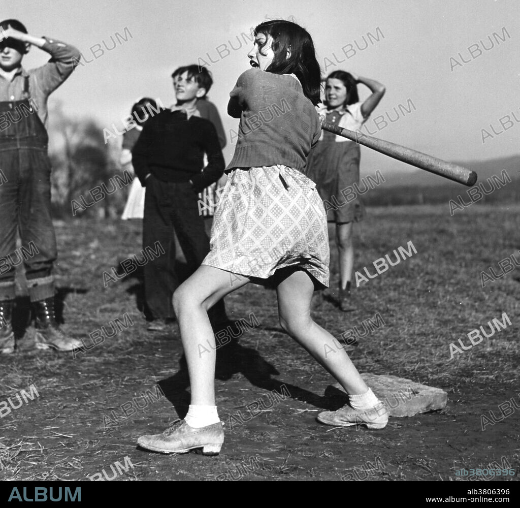 Entitled: "Baseball game, Dailey, West Virginia" showing a girl swinging a baseball bat. Baseball is a bat-and-ball game played between two teams of nine players each who take turns batting and fielding. Evolving from older bat-and-ball games, an early form of baseball was being played in England by the middle of the 18th century. This game was brought by immigrants to North America, where the modern version developed. By the late 19th century, baseball was widely recognized as the national sport of the United States. Baseball is now popular in North America and parts of Central and South America and the Caribbean, East Asia, and Europe. Photographed by Arthur Rothstein, December 1941.