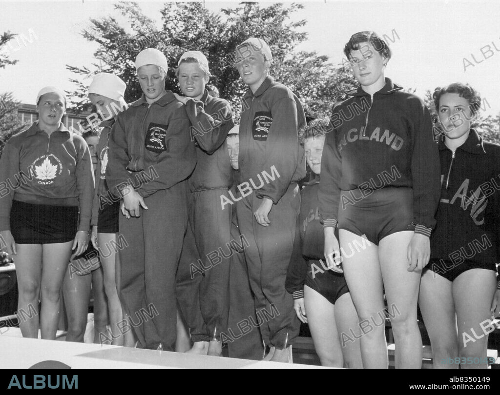 Winners of women's 440-yard freestyle relay swim stand on winner's podium. Left to right: Canadians K. Kemp and V.Grant; Winning team, Joan Harrison, Felicity Loveday, Maggie Petzer (Natalie Myburgh not shown). England's J. Botham and F. Ewart. July 31, 1954. (Photo by Associated Press Photo).