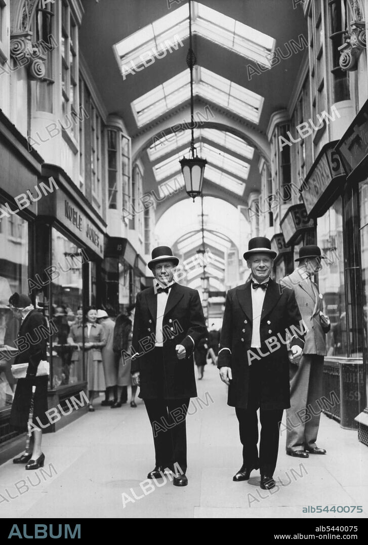 New Uniforms For Burlington Arcade Beadles -- The two beadles, wearing their new uniforms for the first time today, photographed walking in Burlington Arcade. They are (left) Mr. Frank Clark of Fulham and Chief Beadle Robert Baker of Stockwell. The two beadles who, each day at 5-30 pm, ring the 100 - year-old bell for closing time in the famous Burlington Arcade, have just received new uniforms which they will wear during the summer. Made by Sam Fisher, a tailor in the Arcade, using olds prints.