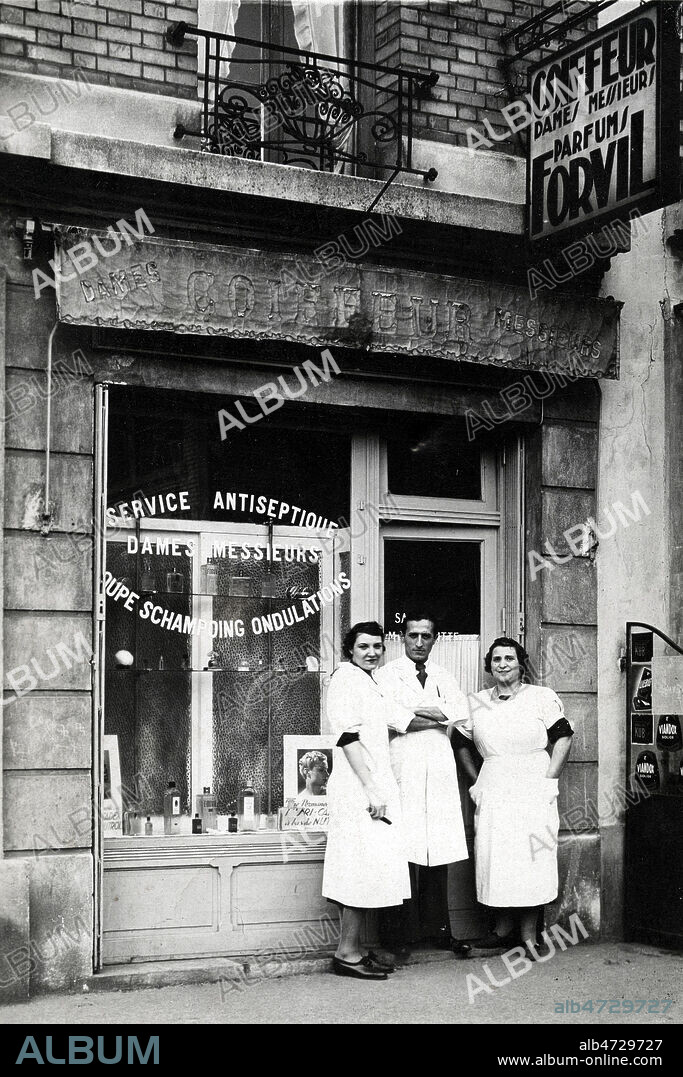 'Service antiseptique. Dames, messieurs. Coupe, shampoing, ondulations'. Devanture d'un salon de coiffure, avec coiffeurs posant. Carte postale vers 1930. Annees 30. Credit : Collection Grob/KHARBINE-TAPABOR.