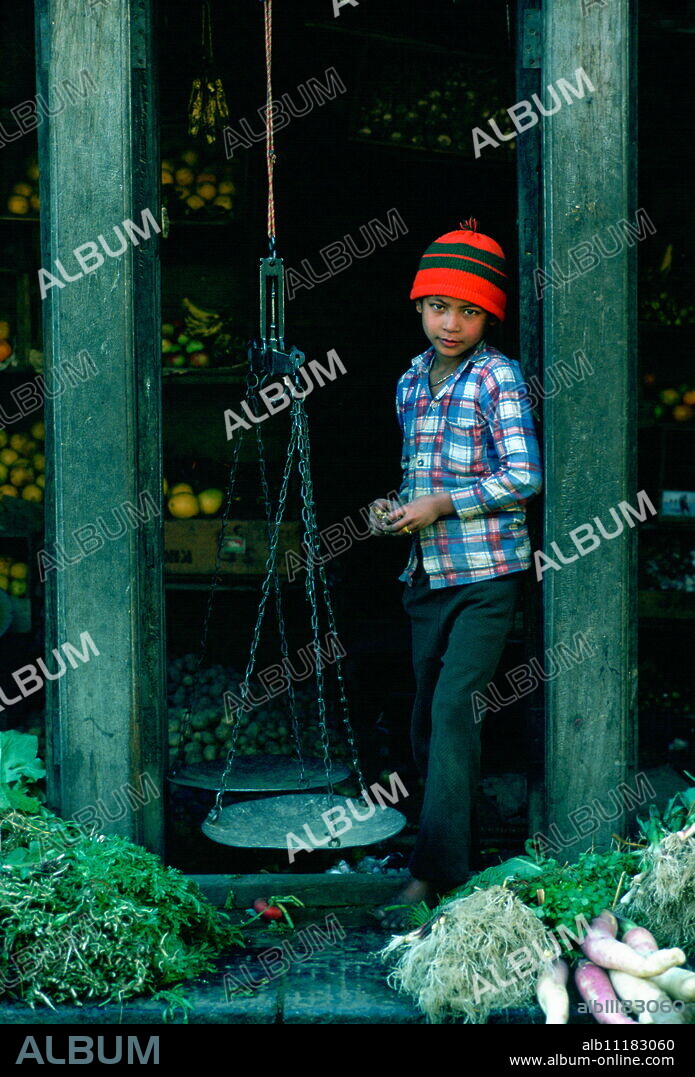Young boy shopkeeper in a fruit and vegetables shop in Patan, Nepal. He has old-fashioned scales for weighing the produce.
