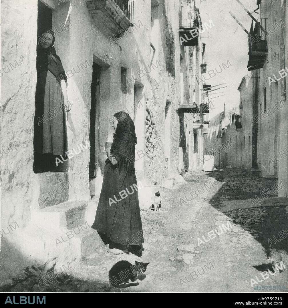 Ibiza, 1935 (CA.). Mujeres hablando en la puerta de una casa, en una calle con gatos.