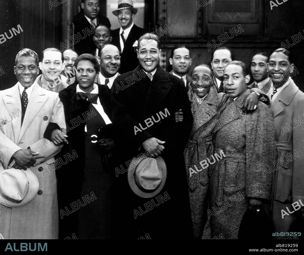 Group portrait of American jazz musician Duke Ellington and his band wearing in overcoats in front of a train, Los Angeles, California. Among those picture are: Harry Carney (far left), Sonny Greer (far right) and Ivie Anderson nex to the Duke. 1934.