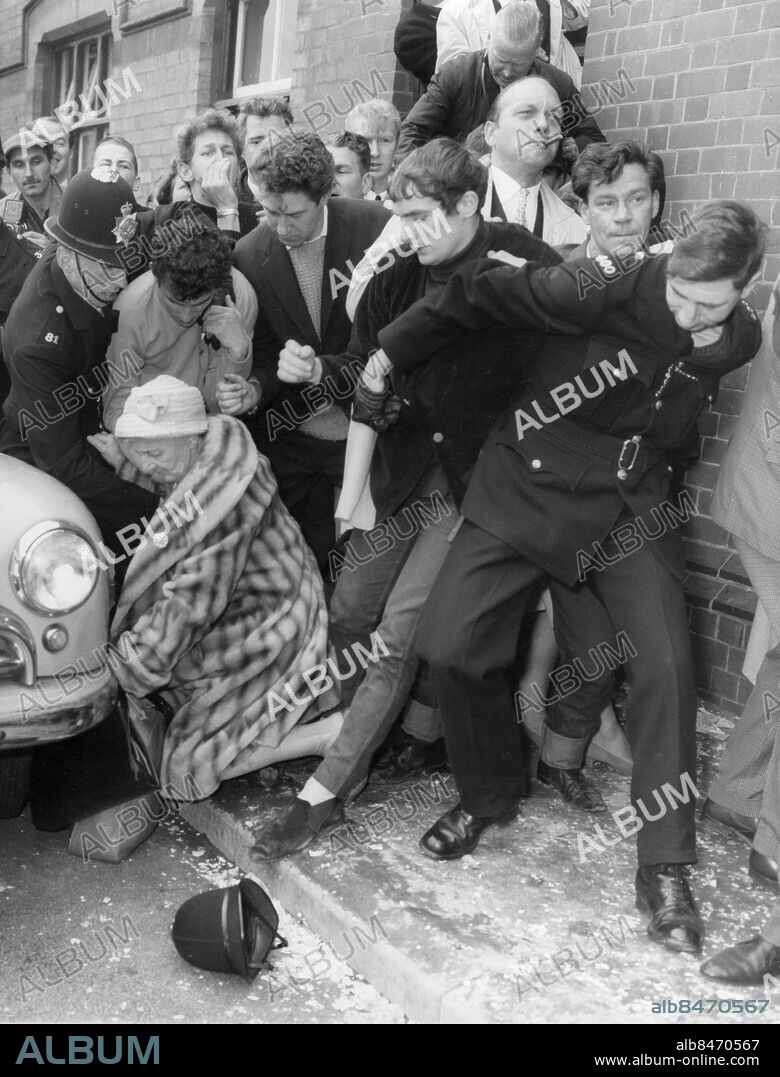 Orig. bildtext... BOOS AT COLIN JORDAN WEDDING A crowd of more than 1,000 gathered outside Coventry Register Office today when Colin Jordan, leader of the National Socialist Movement, married Francois Dior, niece of the late Paris fashion designer. Booing broke out from members of the anti-fascist league who ere in the crowd. Several clods of turf and other missiles were thrown over the heads of police officers at the door. Photo shows: An elderly women is knocked down as the crowd pushes forward whilst a police officers loses his helmet. Anm. Trängsel Upprördhet Nyfikenhet CD82 persons: Colin Jordan* ;Francoise Dior* sites: STORBRITANNIEN.