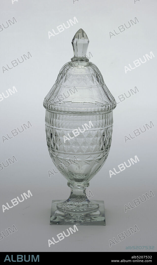 Jar and lid, Glass, Tall urn-shaped body; tapered, fluted stem; square base with star cutting on bottom; tall domed cover with faceted finial; body cut with row of narrow flutes, band of diamonds, a garland circlet, wide flutes down to base; cover cut with conforming pattern; glass greenish and bubly, heavy., Waterford, Ireland, ca. 1800, glasswares, Decorative Arts, Jar and lid.