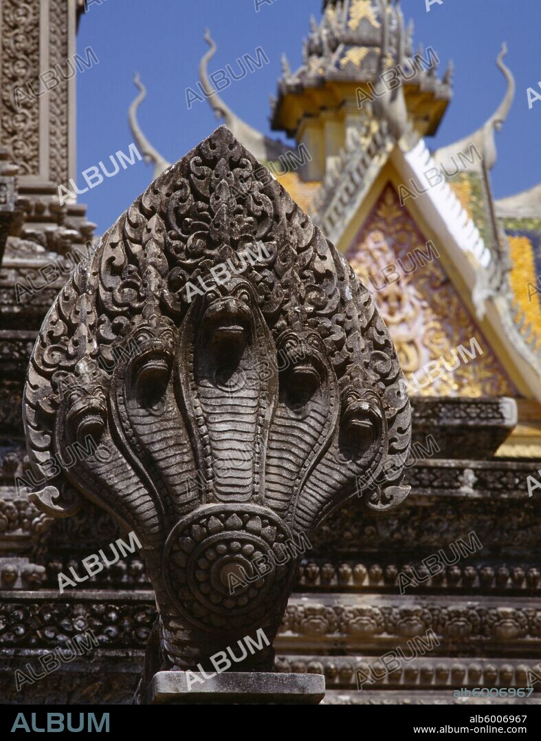 CAMBODIA Phnom Penh Stone carving of naga on temple stupa with roof of Silver Pagoda part seen behind.
