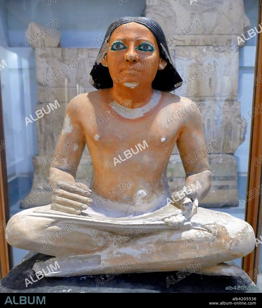 painted limestone statue of an Egyptian scribe seated cross-legged holding an open papyrus scroll. 5th Dynasty. Saqqara.