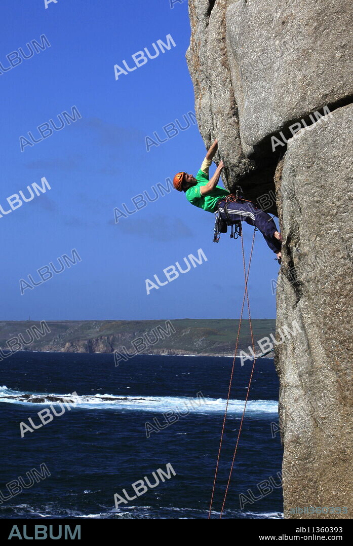 A climber tackles a difficult overhang on the cliffs near Sennen Cove, a popular rock climbing area at Lands End, Cornwall, England, United Kingdom, Europe.