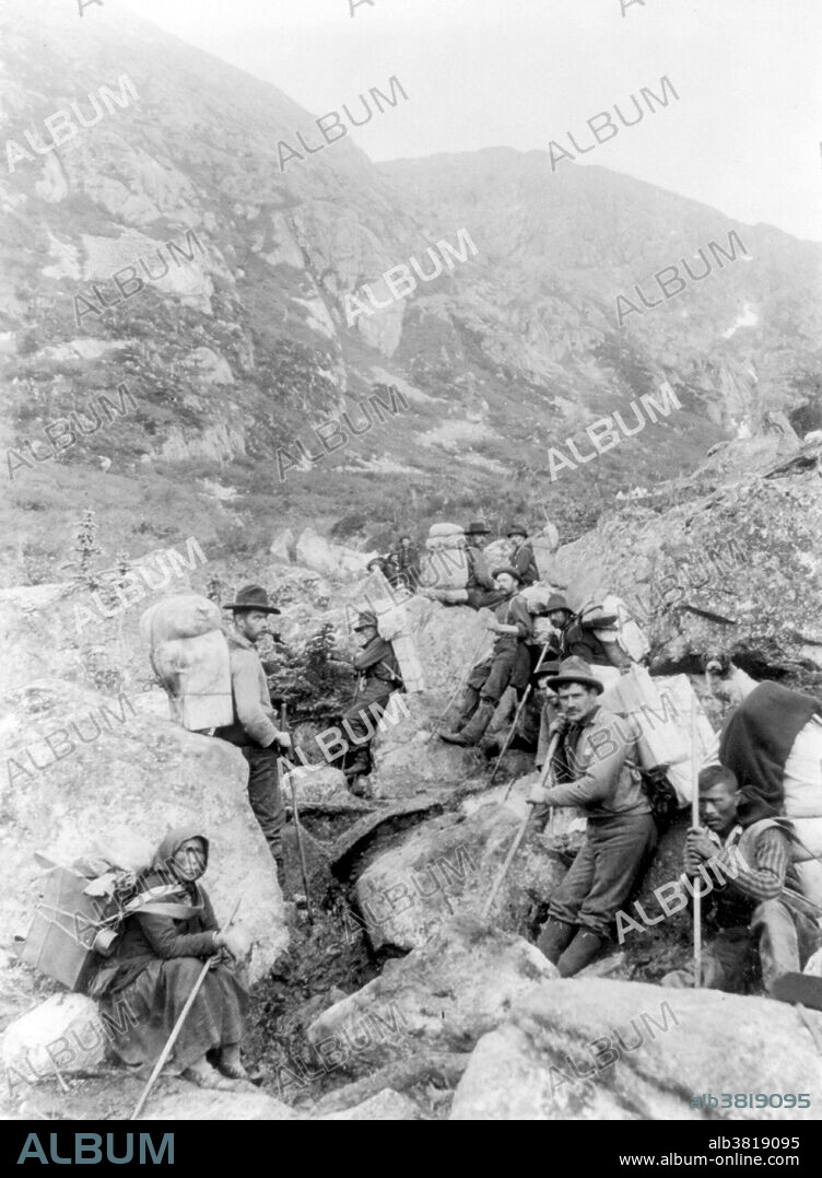 Pack trains on Dyea Trail. The Klondike Gold Rush was a migration by an estimated 100,000 prospectors to the Klondike region of the Yukon between 1896-99. Gold was discovered by local miners on August 16, 1896 and, when news reached Seattle and San Francisco, it triggered a stampede of would-be prospectors. To reach the gold fields most took the route through the ports of Dyea and Skagway in Alaska. Here, the Klondikers could follow either the Chilkoot or the White Pass trails to the Yukon River and sail down to the Klondike. Each of them was required to bring a year's supply of food by the Canadian authorities in order to prevent starvation. In all, their equipment weighed close to a ton, which for most had to be carried in stages by themselves. Together with mountainous terrain and cold climate this meant that those who persisted did not arrive until summer 1898. Mining was challenging as the ore was distributed in an uneven manner and digging was made slow by permafrost. In the summer of 1899, gold was discovered around Nome in west Alaska, and many prospectors left the Klondike for the new goldfields, marking the end of the rush. Gold mining activity lasted until 1903. Photo by LaRoche, 1897.