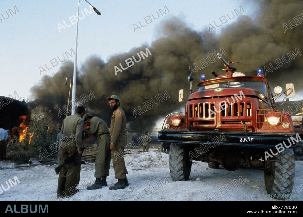 Iran-Irak-Krieg / Erster Golfkrieg (22.09.1980 - 20.08.1988). / Iranische Front / Kriegsschäden. Von irakischen MIGs bei einem Angriff abgefeuerte Raketen entzündeten die Treibstofflager einer Zuckerfabrik, die etwa 30 Kilometer von der irakischen Grenze entfernt liegt. Iranische Soldaten stehen in der Nähe eines Feuerwehrautos, dahinter der dichte Rauch eines brennenden Gastanks. Foto, 11.10.1980.