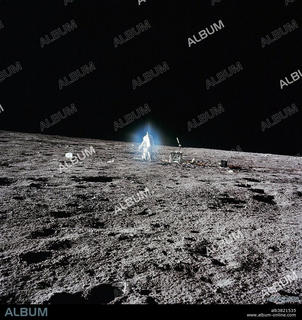 Astronaut Alan L. Bean, lunar module pilot, adjusting the PSE thermal skirt, part of the deployment of the Apollo Lunar Surface Experiments Package (ALSEP) during the first Apollo 12 extravehicular activity (EVA) on November 19, 1969. Bean deployed the ALSEP components 300 feet from the Lunar Module (LM). The blue glow around the subject is possibly due to a dust smudge on the 70mm Hasselblad lens of the lunar surface camera, or lens flare.