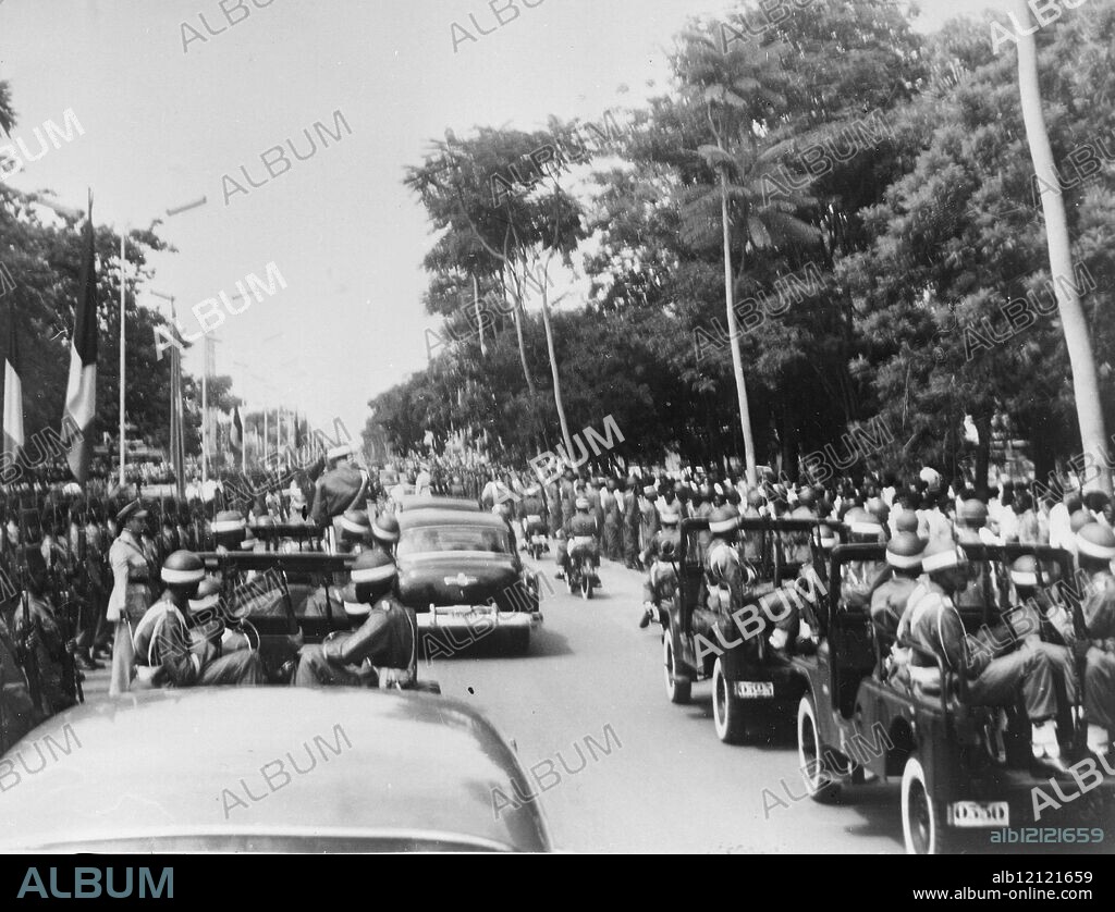 LEOPOLDVILLE - BELGIAN CONGO. KING BAUDOUIN OF BELGIUM MET BY THE LOUDEST PRO-INDEPENDENCE DEMONSTRATION OF HIS CONGO TOUR WHEN HE ARRIVED BY PLANE FROM LULUABOURG. DURING HSI DRIVE FROM THE AIRFIELD ALONG THE WIDE BOULEVARDS OF THE CONGELESE CAPITAL HE WAS ASSAILED BY THUNDEROUS SHOUTS OF "INDEPENDENCE INDEPENDENCE". KING BAUDOUIN IS SEEN HERE IN AN OPEN TOPPED CAR AS WITH AN ESCORT OF MOTORCYCLISTS AND TROOPS LINING THE ROAD HE DROVE THROUGH LEOPOLDVILLE. 28 DECEMBER 1959.