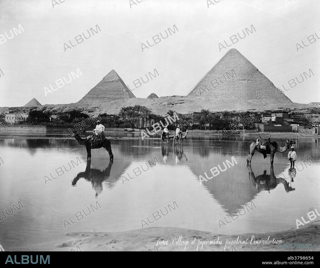 Entitled: "Village and pyramids during the flood-time, circa 189?". shows men on camels and one man standing next to a camel in shallow flood water, with pyramids in the background. The Giza Necropolis (pyramids of Giza) is an archeological site on the Giza Plateau, on the outskirts of Cairo, Egypt. This complex of ancient monuments includes the three pyramid complexes known as the Great Pyramids, the massive sculpture known as the Great Sphinx, several cemeteries, a workers' village and an industrial complex. The pyramids, which have historically loomed large as emblems of ancient Egypt in the Western imagination, were popularized in Hellenistic times, when the Great Pyramid was listed by Antipater of Sidon as one of the Seven Wonders of the World. It is by far the oldest of the ancient Wonders and the only one still in existence. Photographed by Maison Bonfils, 1890s.