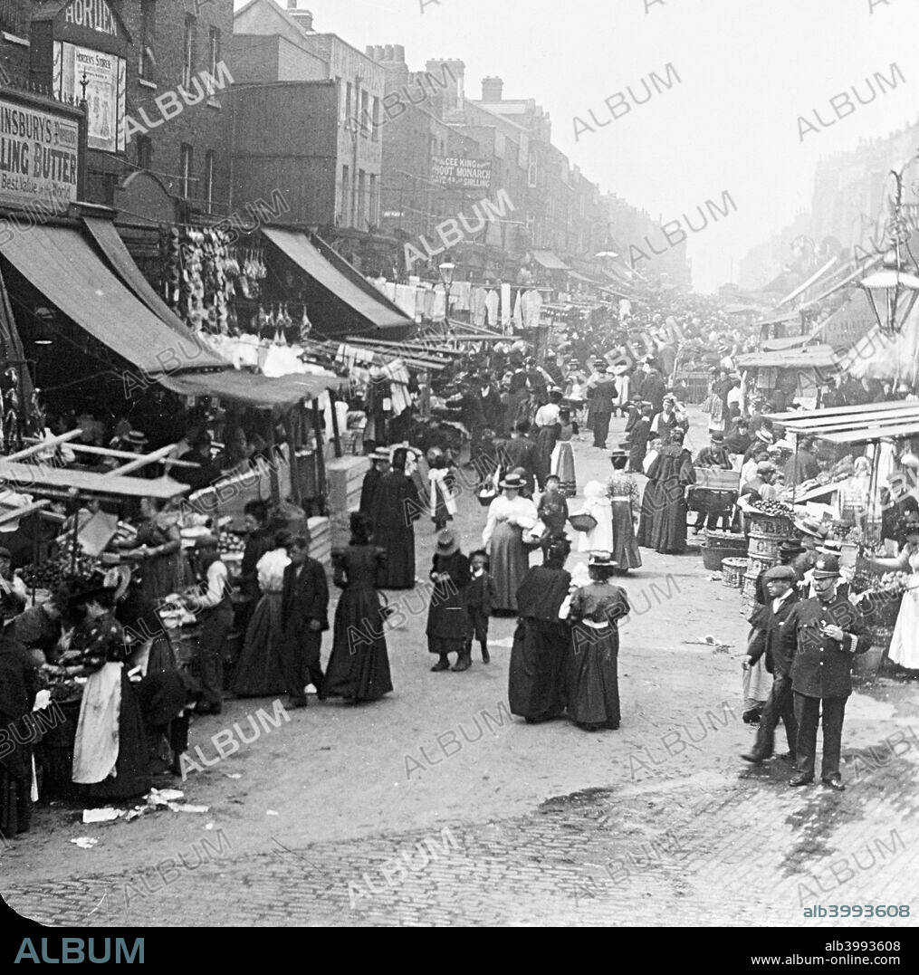 Chapel Market, Islington, London. The street is lined with market stalls and shops, and is bustling with shoppers. A policeman keeps an eye on things in the bottom right corner.