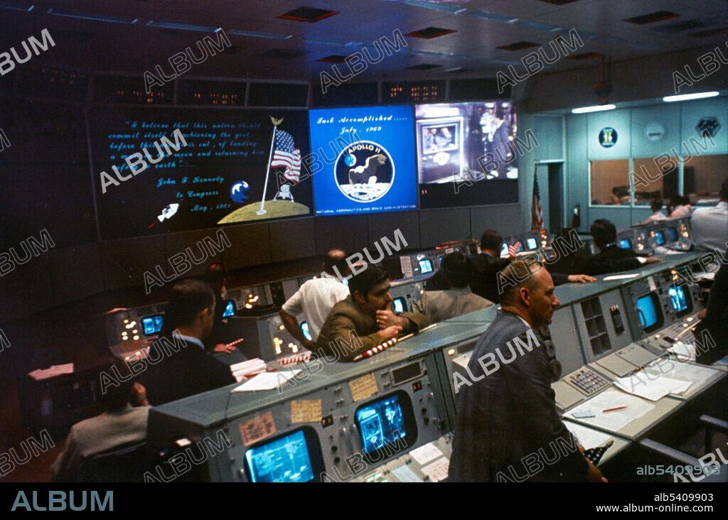 Overall view of the Mission Operations Control Room (MOCR) in the Mission Control Center (MCC), Building 30, Manned Spacecraft Center (MSC), at the conclusion of the Apollo 11 lunar landing mission. The television monitor shows President Richard M. Nixon greeting the Apollo 11 astronauts aboard the USS Hornet in the Pacific recovery area. Astronauts Neil A. Armstrong, Michael Collins, and Edwin E. Aldrin Jr. are inside the Mobile Quarantine Facility (MQF).