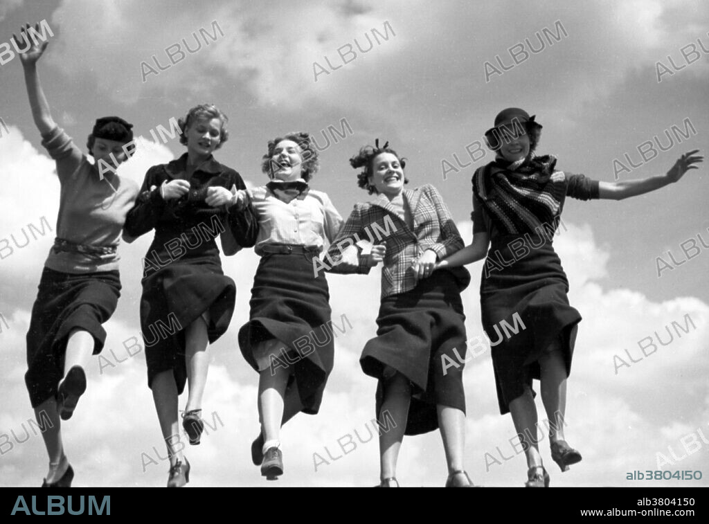 Entitled: "Five women holding hands and walking together in a row, sky in background" photographed by Toni Frissell for Vogue Magazine August 1935. Fashion is a distinctive and often habitual trend in the style in which a person dresses. It is the prevailing styles in behavior and the newest creations of textile designers. Prior to the mid-19th century, most clothing was custom-made. It was handmade for individuals, either as home production or on order from dressmakers and tailors. By the beginning of the 20th century, with the rise of new technologies such as the sewing machine, the development of the factory system of production, and the emergence of department stores, clothing had increasingly come to be mass-produced in standard sizes and sold at fixed prices.