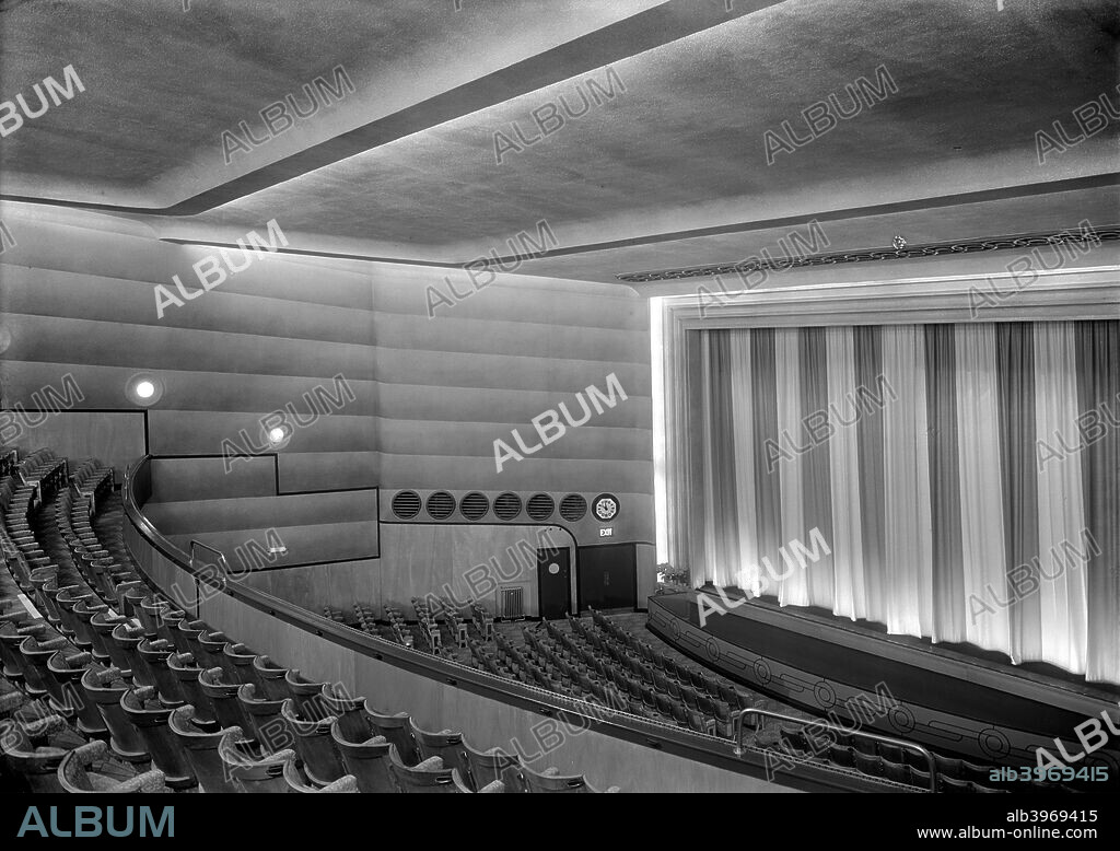 Auditorium of the Odeon, Well Hall Road, Eltham, London, 1936. The cinema was opened in 1936 to the designs of Andrew Mather, an architect specialising in cinema commissions. Circular features relieve a strong linear emphasis, a typical Art Deco combination. The seating is divided into an upper and a lower level, and the curtains are drawn to cover the screen.