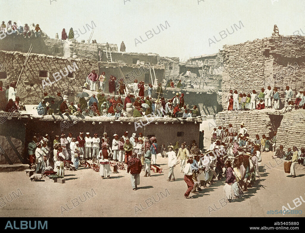 Zuni Indian men doing the Rain Dance as people watch from surrounding buildings in Zuni Pueblo, New Mexico, 1899. Photochrom color print.