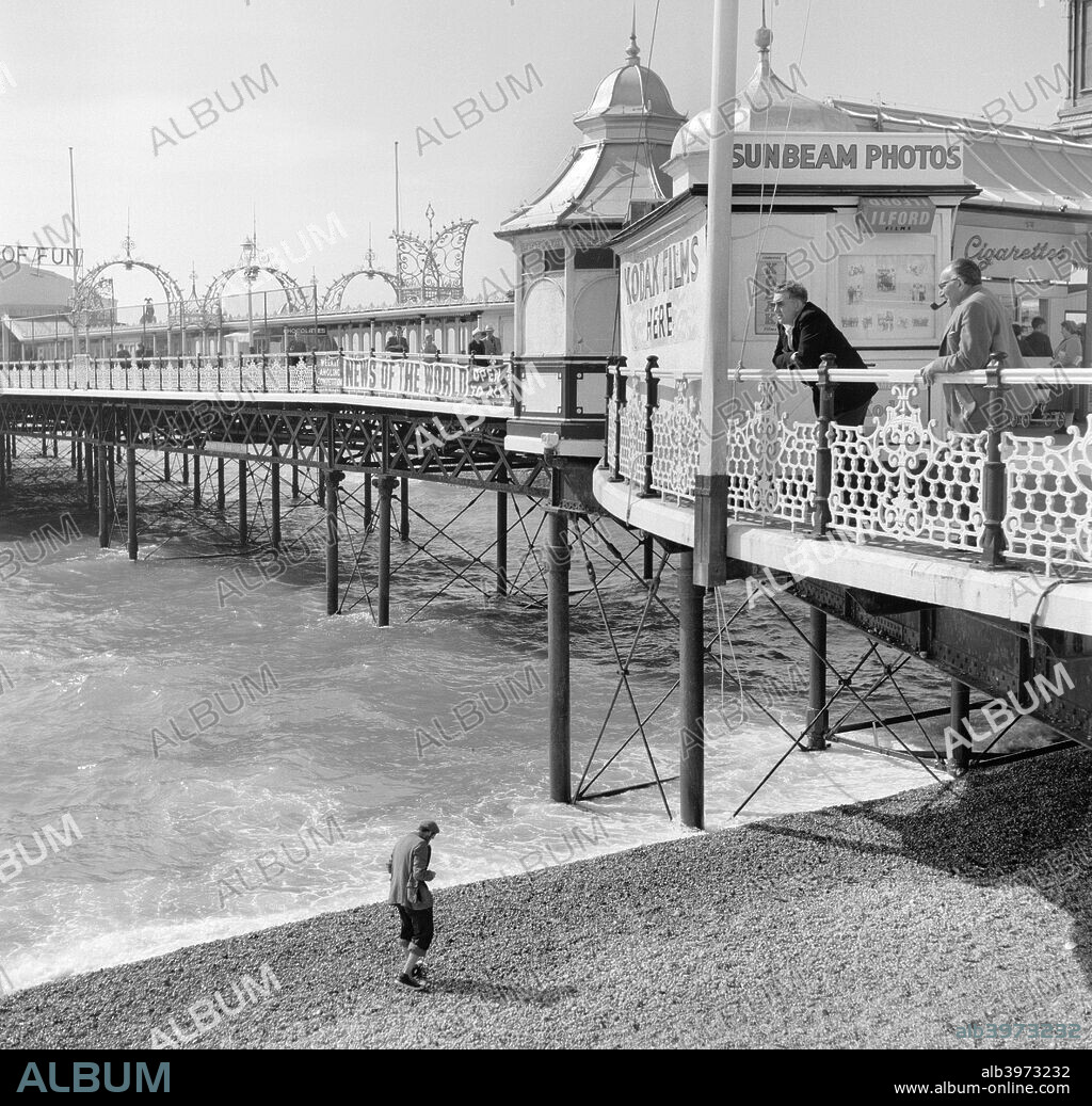 Palace Pier, Brighton, East Sussex, 1960s. Holidaymakers lean on the railing outside a kiosk and photo booth on the Palace Pier which was built between 1891-1899.