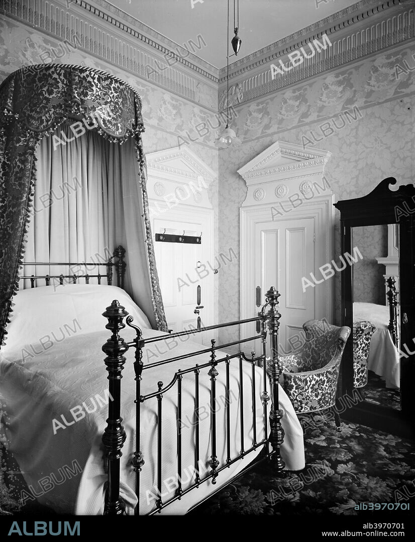 A bedroom in the Hotel Cecil, The Strand, London. The double bed has a brass bedstead and a decorative canopy.