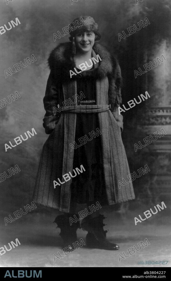 Young flapper girl wearing long coat with fur collar, cap and boots, 1922. Flappers were a new breed of young Western women in the 1920's who wore short skirts, bobbed their hair, listened to jazz, and flaunted their disdain for what was then considered acceptable behavior. Flappers were seen as brash for wearing excessive makeup, drinking, treating sex in a casual manner, smoking, driving automobiles and otherwise flouting social and sexual norms. Flappers had their origins in the period of Liberalism, social and political turbulence and increased transatlantic cultural exchange that followed the end of World War I, as well as the export of American jazz culture to Europe.