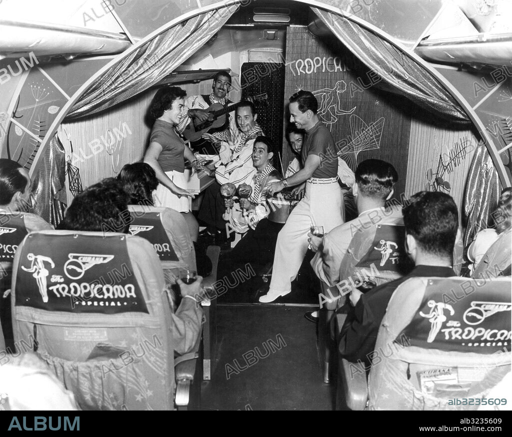 Orig. bildtext... FÖRSTA FLYGANDE NATTKLUBBEN. Kubas flygbolag Cubana de Aviacion är det första som bjuder sina passagerare på komplett nattklubb ombord. Bolaget har specialinrett sin stora Super G Constellations till nattklubben Tropicana och där spelar på linjen Miami till Havnna välkända mambobandet Gloria Ann och Orlando, orkestern har t.o.m. pianot med sig ombord. Mellan champagneklunkarna tar då och då folket en svängom i luftgroparna. Sånt kallas service, nu undras bara när SAS kommer efter med allmogelåtar på väg till Los Angeles. Anm. Ryggbilder sites: CUBA ;USA.