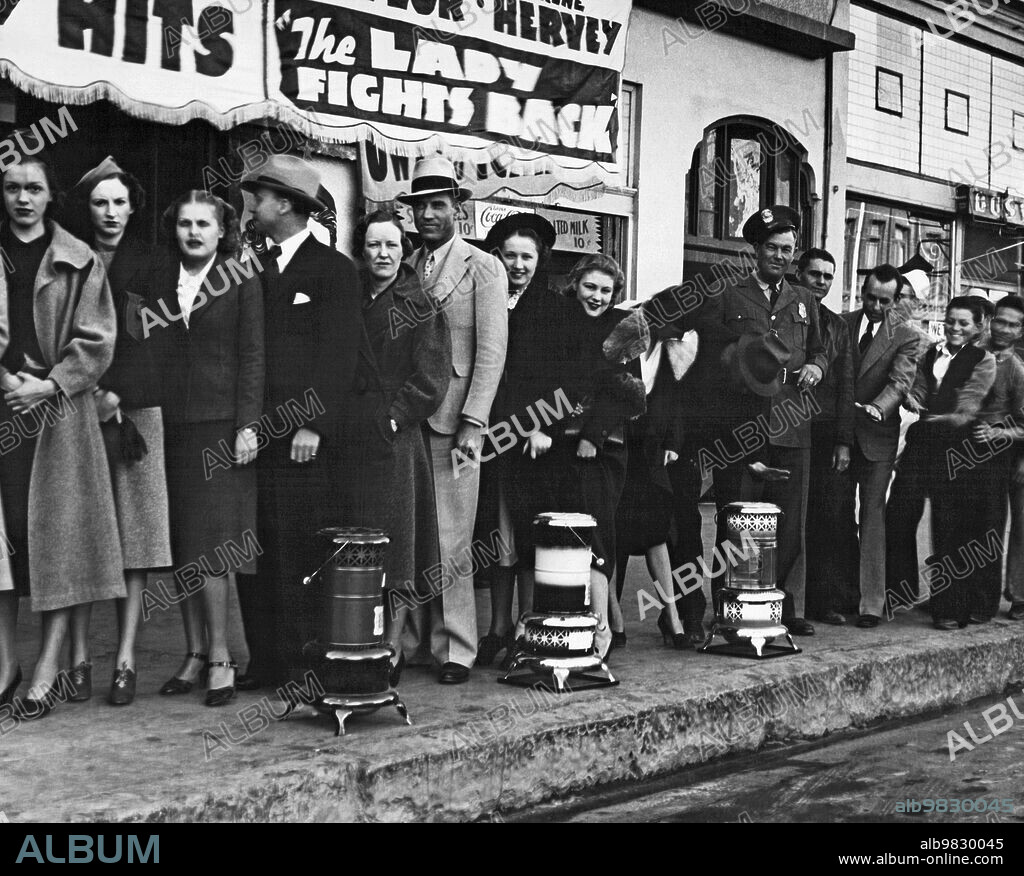Phoenix, Arizona: circa December, 1937, Movie fans waiting in queue to enter the Rialto Theater. The manager of the theater has put out oil stoves in front of the building, therefore making his customers quite comfortable while waiting to enter in the winter.