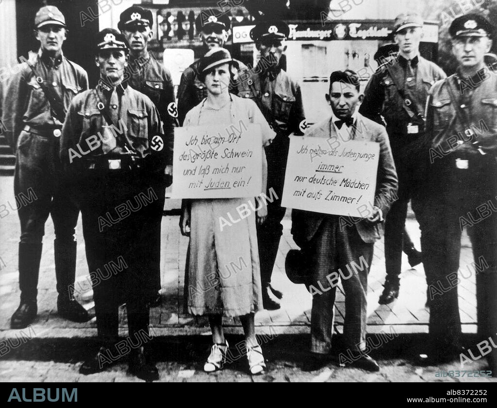 The woman's sign reads: 'I am the biggest pig in the town and only get involved with Jews!', and the man's sign reads: 'As a Jewish boy, I only go to bed with German girls'. The man is thought to be Oskar Dankner, owner of a cinema in Cuxhaven.