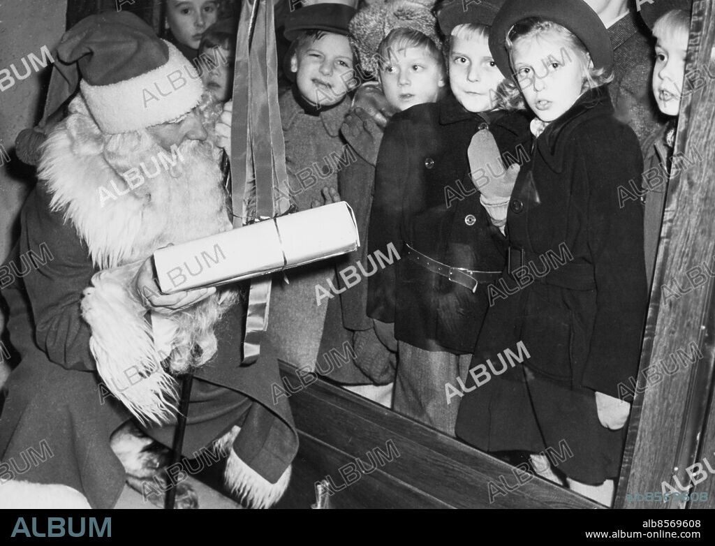 Orig. bildtext... SKYLTSÖNDAG. NK:s tomte väckte livligt intresse hos de unga flanörerna, här ses nyfikna beundrare. Anm. Jultomtar Tomtar Julklappar Syskon sites: STOCKHOLM ;SVERIGE.