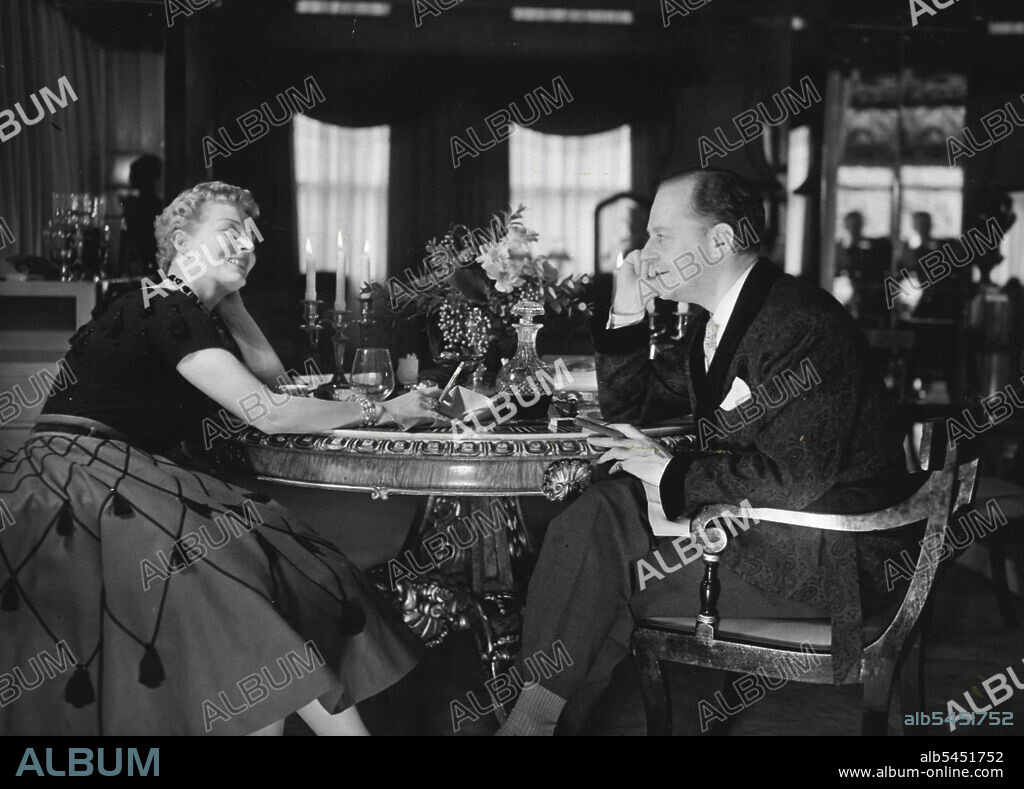 Digby Morton And Ann Seymour At Home -- Digby Morton, the London Fashion Designer, and Mrs. Morton who is better known under her pen name Ann Seymour as the writer on beauty culture and on fashions. They are photograhed after dinner in their elegant London pent-house. July 20, 1954. (Photo by Camera Press).