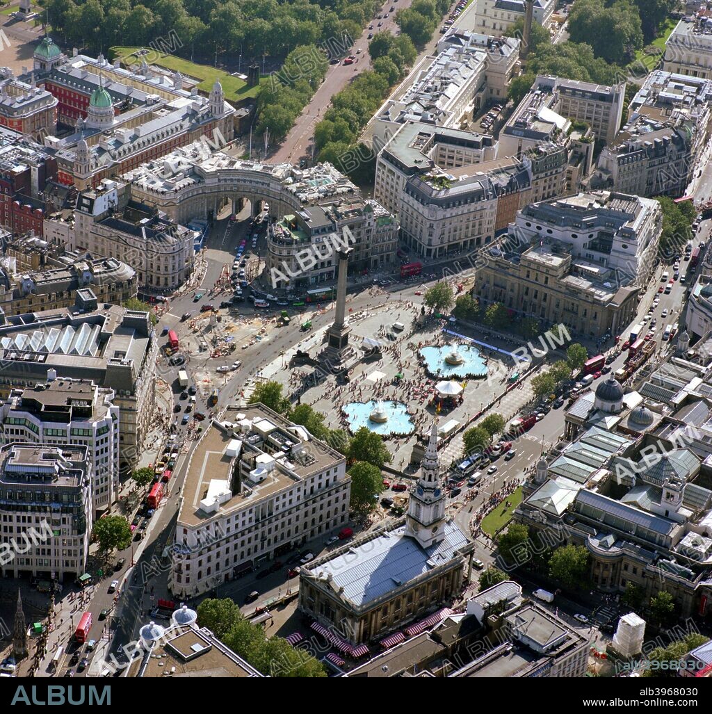Trafalgar Square, Westminster, London, 2002.This picture was taken from above The Strand. To the bottom left is the 1865 replica of the original Charing Cross. Right of this are South Africa House and the Church of St Martin-in-the-Fields, while straight up past Trafalgar Square is Admiralty Arch, under which The Mall leads to Buckingham Palace. To the far right of the picture is the National Gallery.